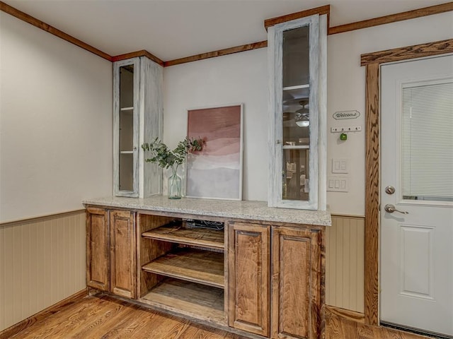 bar with a wainscoted wall, wood walls, and light wood finished floors