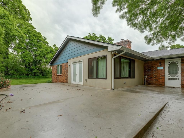 rear view of property with french doors, a chimney, a patio area, and brick siding