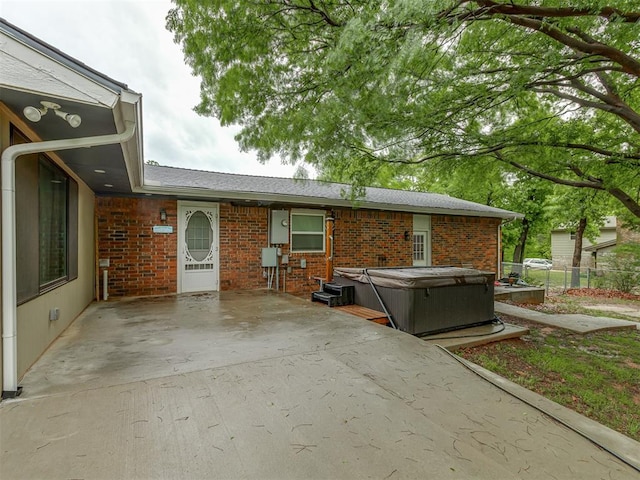 exterior space with brick siding, a hot tub, and a patio area