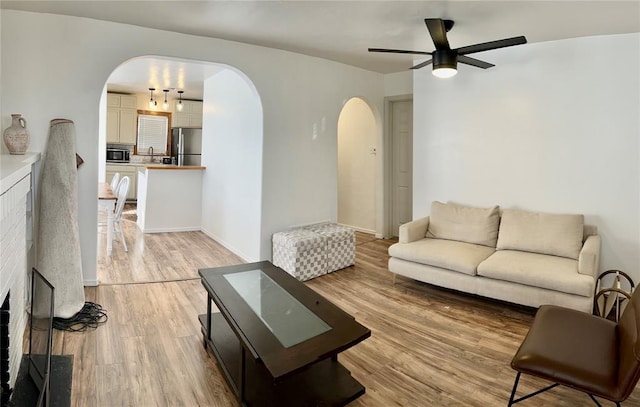 living area with arched walkways, ceiling fan, and light wood-type flooring