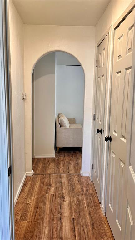 hallway featuring arched walkways, baseboards, and wood finished floors