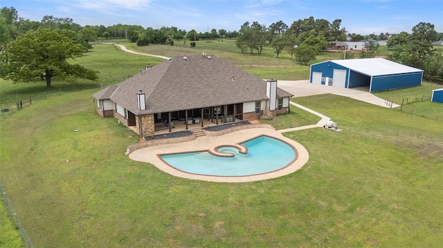 view of swimming pool with a lawn, a pool with connected hot tub, an outbuilding, fence, and a pole building