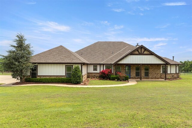 view of front facade with brick siding, a front lawn, and roof with shingles