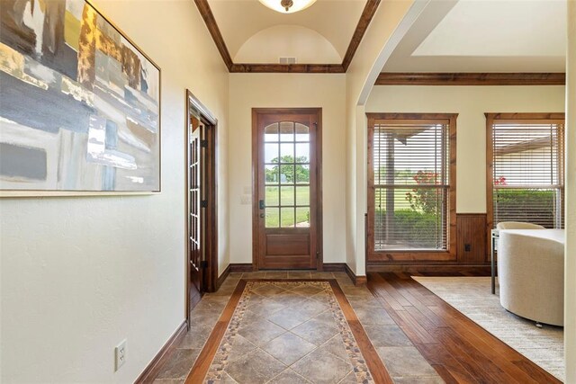 entryway with crown molding, arched walkways, baseboards, and lofted ceiling