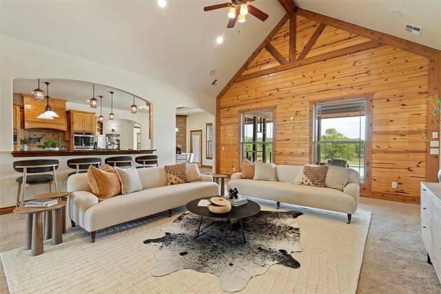 living area featuring ceiling fan, visible vents, arched walkways, high vaulted ceiling, and wooden walls