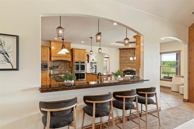 kitchen with backsplash, stainless steel double oven, arched walkways, a peninsula, and recessed lighting