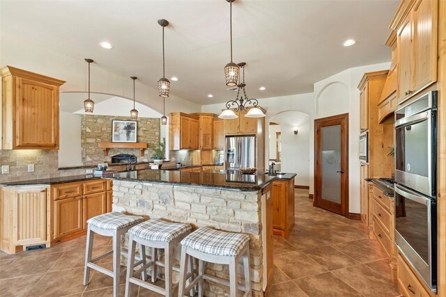 kitchen featuring decorative backsplash, pendant lighting, a kitchen island, arched walkways, and appliances with stainless steel finishes