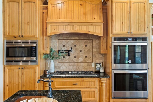 kitchen with a sink, dark stone countertops, stainless steel appliances, decorative backsplash, and custom exhaust hood