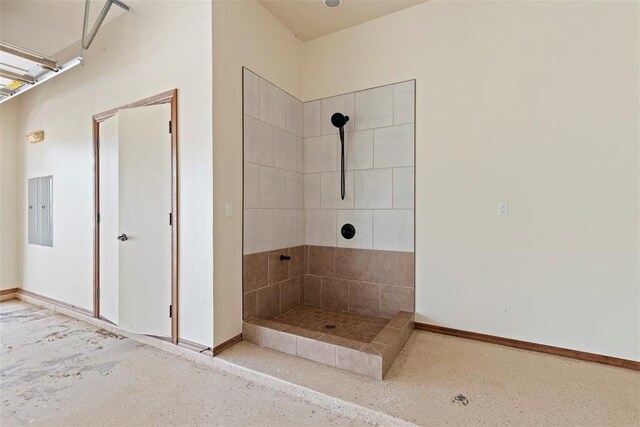 bathroom with baseboards, a tile shower, and electric panel