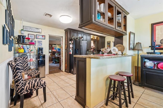5720 12th Ave NW, Norman, OK 73069 - kitchen featuring stainless steel fridge, light tile patterned floors, glass insert cabinets, a breakfast bar, and stone counters