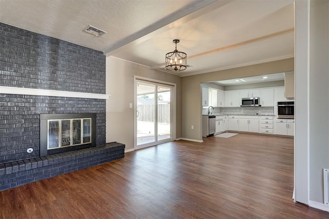 1508 Carlton Way, Oklahoma City, OK 73120 - unfurnished living room featuring an inviting chandelier, visible vents, a brick fireplace, baseboards, and dark wood finished floors