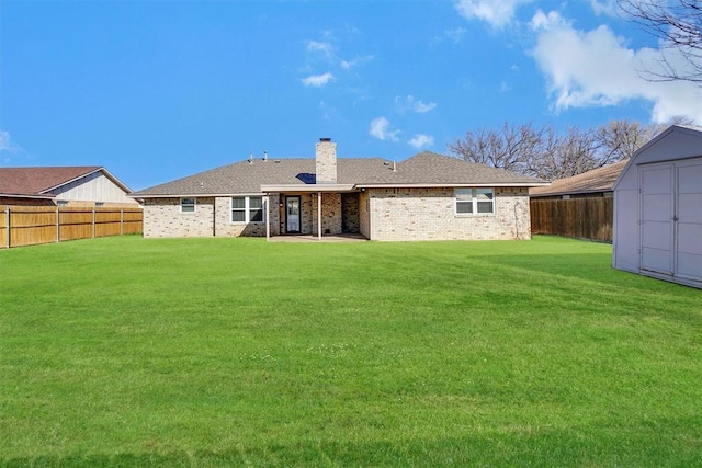 rear view of house with a fenced backyard, a storage unit, a chimney, and a lawn