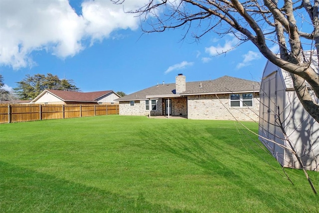 rear view of property with a yard, brick siding, a chimney, and a fenced backyard