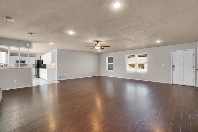 unfurnished living room with a textured ceiling, ceiling fan, visible vents, and dark wood-style floors