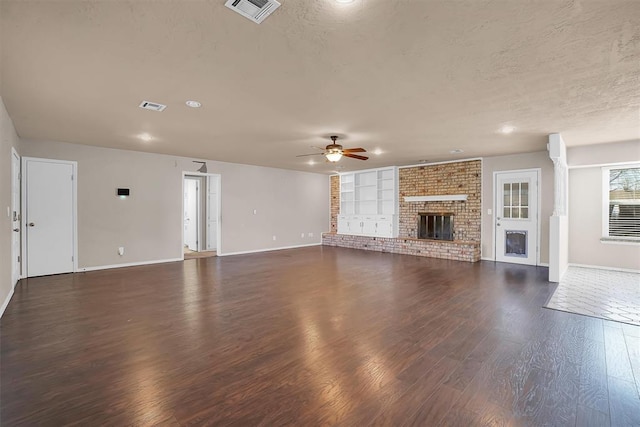 unfurnished living room featuring ceiling fan, a brick fireplace, baseboards, visible vents, and dark wood-style floors