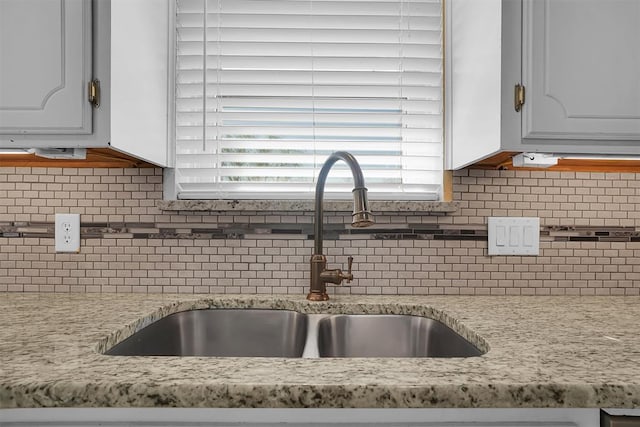 kitchen featuring a sink, light stone countertops, backsplash, and white cabinetry