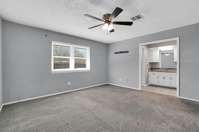 unfurnished bedroom featuring visible vents, baseboards, light colored carpet, connected bathroom, and a textured ceiling