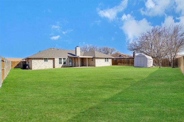 back of property with a chimney, a lawn, an outbuilding, a fenced backyard, and a storage unit