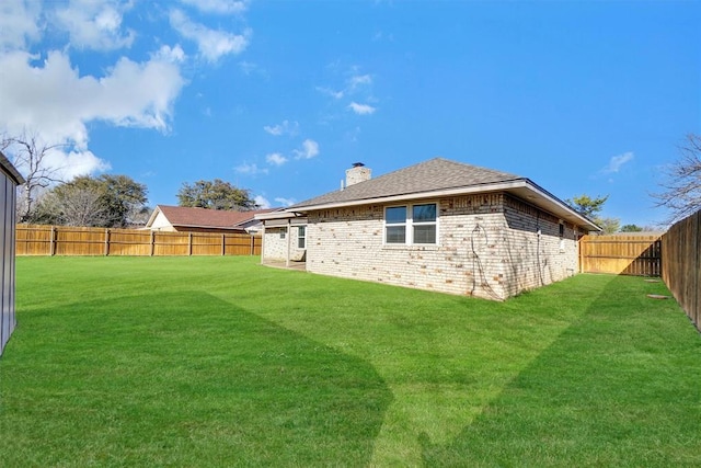 back of property with roof with shingles, brick siding, a fenced backyard, a chimney, and a lawn