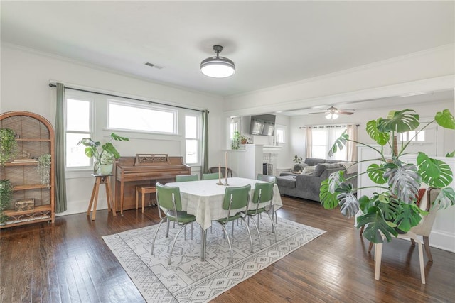 dining space featuring a fireplace, visible vents, ornamental molding, and dark wood-type flooring