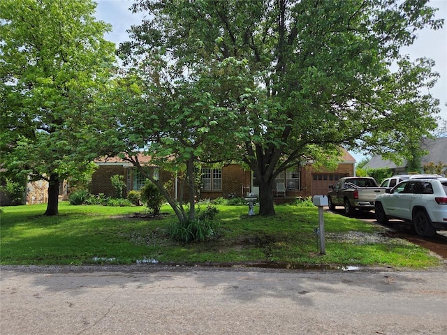 obstructed view of property with a garage, brick siding, and a front yard