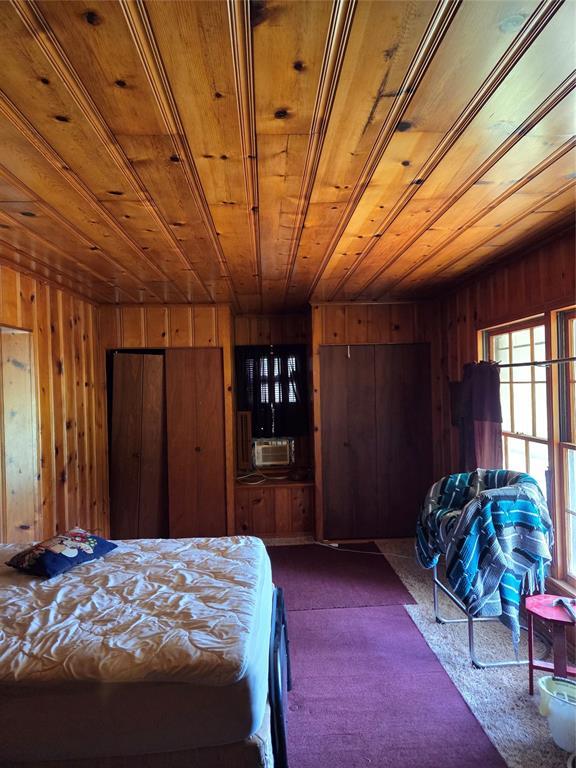 bedroom featuring wooden walls, wood ceiling, and dark carpet