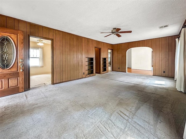 903 Sunset Dr, El Reno, OK 73036 - unfurnished living room with ceiling fan, visible vents, arched walkways, wood walls, and carpet floors