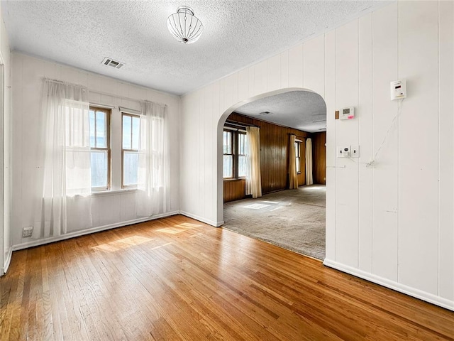 903 Sunset Dr, El Reno, OK 73036 - empty room with wooden walls, arched walkways, a textured ceiling, visible vents, and hardwood / wood-style flooring