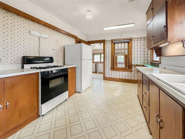 903 Sunset Dr, El Reno, OK 73036 - kitchen with light countertops, freestanding refrigerator, wallpapered walls, light floors, and gas range oven