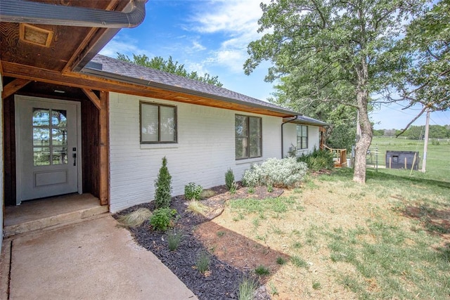 view of property exterior featuring a lawn, a shingled roof, fence, and brick siding