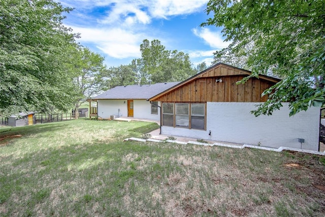 back of property featuring an outdoor structure, fence, brick siding, a lawn, and a storage shed