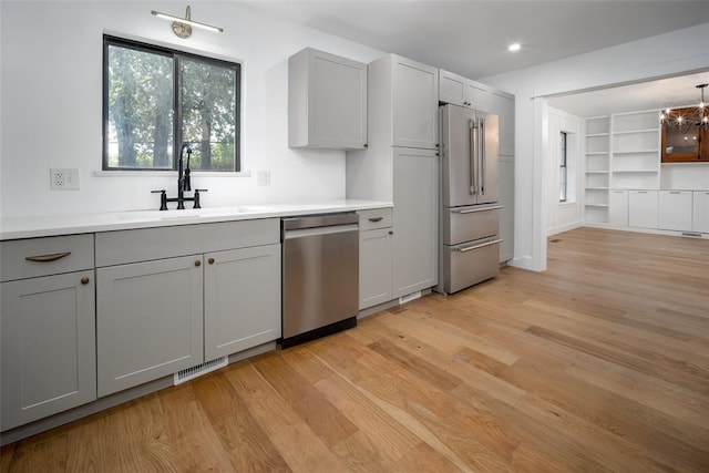 kitchen featuring appliances with stainless steel finishes, a sink, gray cabinets, light wood-type flooring, and visible vents