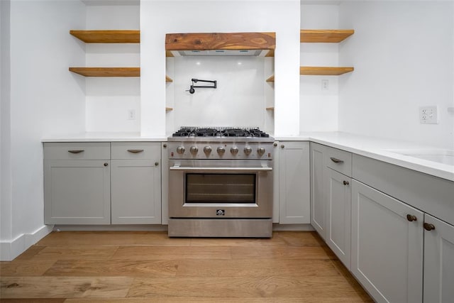 kitchen with open shelves, stainless steel stove, light wood finished floors, light countertops, and gray cabinets