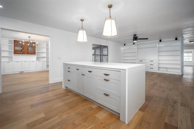 kitchen with light wood-style floors, light countertops, built in shelves, ceiling fan with notable chandelier, and pendant lighting