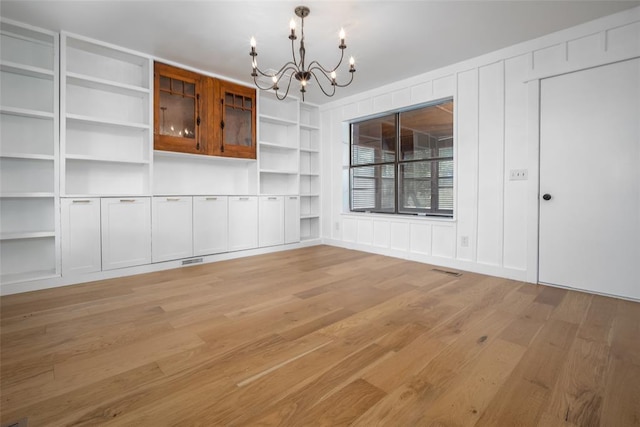 unfurnished dining area featuring light wood-style floors, built in features, a chandelier, and visible vents