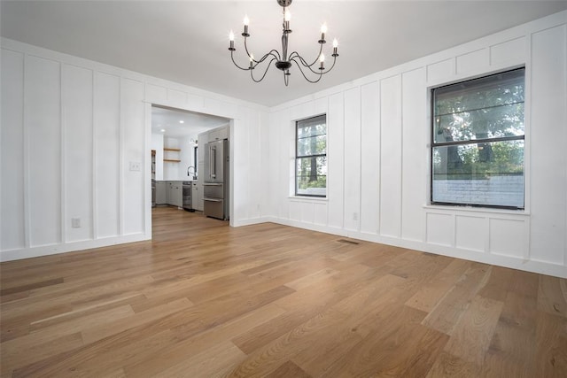 unfurnished dining area with an inviting chandelier, visible vents, a decorative wall, a sink, and light wood-style flooring