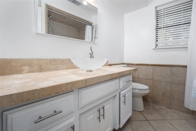 bathroom featuring visible vents, vanity, toilet, tile walls, and a wainscoted wall