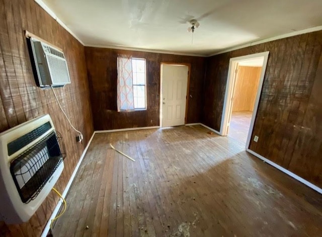 interior space with ornamental molding, heating unit, wooden walls, and hardwood / wood-style flooring