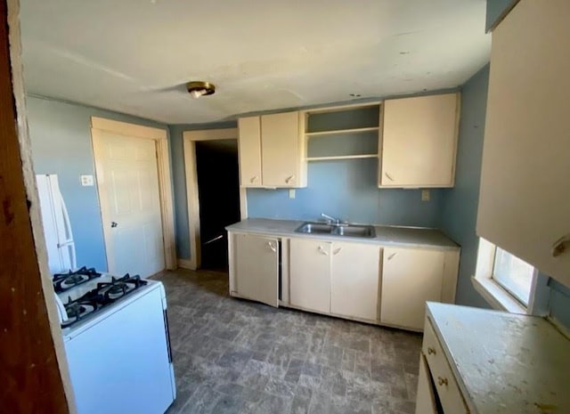 kitchen featuring open shelves, dishwashing machine, white gas range, light countertops, and a sink