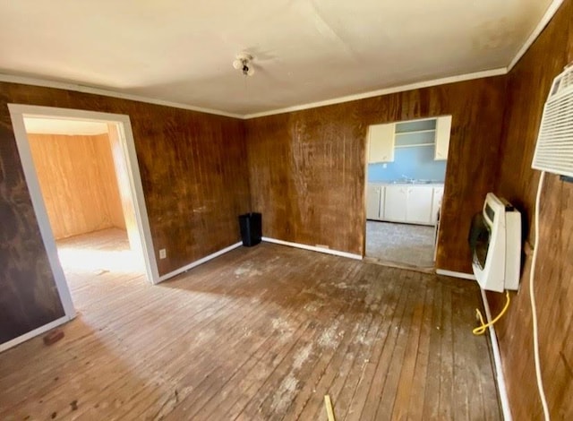 empty room with crown molding, heating unit, wooden walls, and hardwood / wood-style flooring