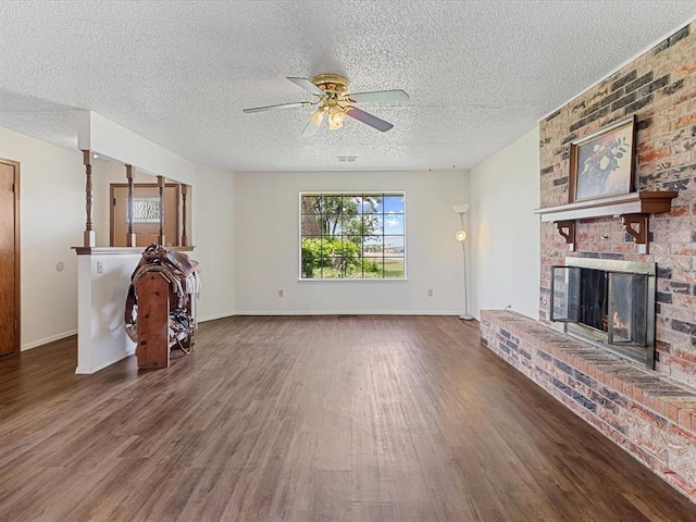 unfurnished living room featuring wood finished floors, ceiling fan, a brick fireplace, a textured ceiling, and baseboards