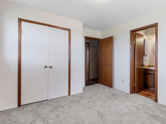unfurnished bedroom featuring carpet, a closet, a textured ceiling, baseboards, and ensuite bath