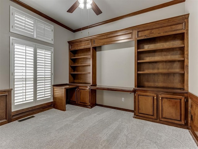 interior space featuring crown molding, visible vents, light colored carpet, built in desk, and a ceiling fan
