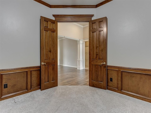 carpeted empty room featuring crown molding, decorative columns, and a wainscoted wall