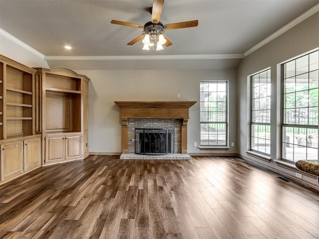 unfurnished living room featuring ceiling fan, crown molding, a brick fireplace, dark wood finished floors, and baseboards