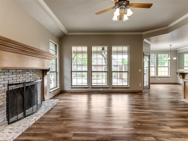 unfurnished living room with crown molding, a brick fireplace, dark wood finished floors, baseboards, and ceiling fan with notable chandelier