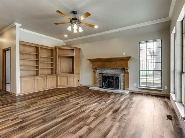 unfurnished living room featuring a fireplace with raised hearth, dark wood finished floors, a ceiling fan, visible vents, and ornamental molding