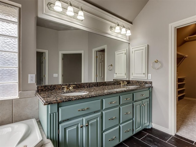 full bath with double vanity, lofted ceiling, a walk in closet, a tub, and a sink