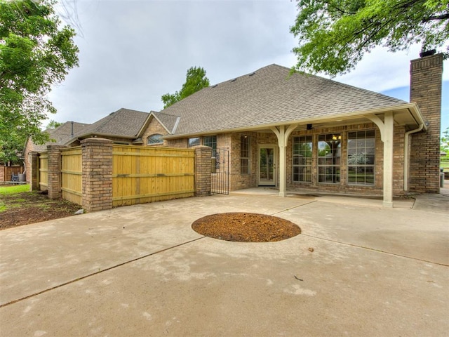 exterior space featuring roof with shingles, fence, brick siding, a gate, and a chimney