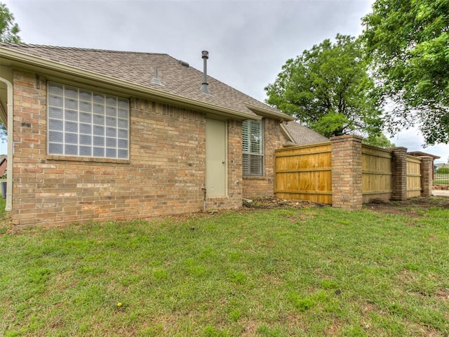 rear view of property featuring a yard, brick siding, fence, and a shingled roof